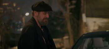 Movie still from “10 Days of a Bad Man” (2023), directed by Uluç Bayraktar – A man with a beard wearing a hat and a jacket; Close Up shot, Over the shoulder angle