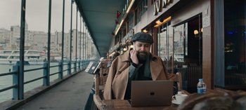 Movie still from “10 Days of a Bad Man” (2023), directed by Uluç Bayraktar – A man sitting in front of a laptop computer; Medium shot, High angle