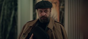 Movie still from “10 Days of a Bad Man” (2023), directed by Uluç Bayraktar – A man with a beard wearing a hat and a jacket; Close Up shot, Low angle