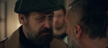 Movie still from “10 Days of a Bad Man” (2023), directed by Uluç Bayraktar – A man with a beard and a hat is talking to another man; Close Up shot, Over the shoulder angle