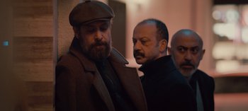 Movie still from “10 Days of a Bad Man” (2023), directed by Uluç Bayraktar – A man in a brown coat and a man in a brown hat; Medium shot, Low angle