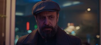 Movie still from “10 Days of a Bad Man” (2023), directed by Uluç Bayraktar – A man with a beard wearing a hat and a jacket; Close Up shot, Low angle