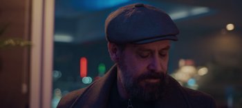 Movie still from “10 Days of a Bad Man” (2023), directed by Uluç Bayraktar – A man with a beard wearing a hat and a coat; Close Up shot, Low angle