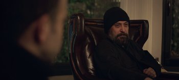 Movie still from “10 Days of a Bad Man” (2023), directed by Uluç Bayraktar – A man sitting in a leather chair with a beard; Medium shot, Over the shoulder angle