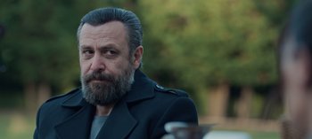 Movie still from “10 Days of a Bad Man” (2023), directed by Uluç Bayraktar – A man with a beard wearing a jacket; Close Up shot, Over the shoulder angle