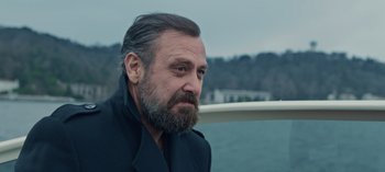 Movie still from “10 Days of a Bad Man” (2023), directed by Uluç Bayraktar – A man with a beard and a jacket on looking out at the water; Close Up shot, Low angle