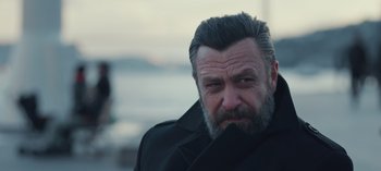 Movie still from “10 Days of a Bad Man” (2023), directed by Uluç Bayraktar – A person with a beard wearing a black coat; Close Up shot, Over the shoulder angle
