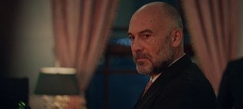 Movie still from “10 Days of a Bad Man” (2023), directed by Uluç Bayraktar – A man in a suit and tie looking at the camera; Close Up shot, Low angle