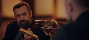 Movie still from “10 Days of a Bad Man” (2023), directed by Uluç Bayraktar – A man with a beard is holding a pipe; Close Up shot, Over the shoulder angle