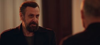Movie still from “10 Days of a Bad Man” (2023), directed by Uluç Bayraktar – A man with a goatee and beard wearing a jacket; Close Up shot, Over the shoulder angle