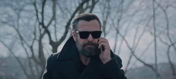 Movie still from “10 Days of a Bad Man” (2023), directed by Uluç Bayraktar – A man with a beard is talking on a cell phone; Close Up shot, Low angle