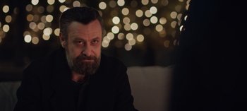 Movie still from “10 Days of a Bad Man” (2023), directed by Uluç Bayraktar – A man with a goatee sitting in front of lights; Close Up shot, Over the shoulder angle