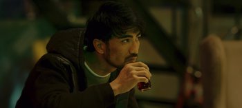 Movie still from “10 Days of a Bad Man” (2023), directed by Uluç Bayraktar – A man with a beard is holding a drink; Close Up shot, High angle