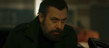 Movie still from “10 Days of a Bad Man” (2023), directed by Uluç Bayraktar – A person with a beard wearing a jacket; Close Up shot, Low angle