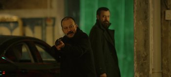 Movie still from “10 Days of a Bad Man” (2023), directed by Uluç Bayraktar – A man holding a gun while standing next to another man; Medium shot, Low angle