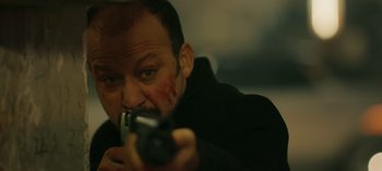 Movie still from “10 Days of a Bad Man” (2023), directed by Uluç Bayraktar – A man holding a gun while wearing a black jacket; Close Up shot, Low angle