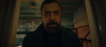 Movie still from “10 Days of a Bad Man” (2023), directed by Uluç Bayraktar – A person with a beard looking at the camera; Close Up shot, Low angle