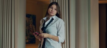 Movie still from “10 Days of a Good Man” (2023), directed by Uluç Bayraktar – A woman in a white shirt and a black tie holding a cell phone; Medium shot, Low angle