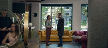 Movie still from “10 Days of a Good Man” (2023), directed by Uluç Bayraktar – Two people standing in front of a yellow couch in front of a window; Wide shot, Over the shoulder angle