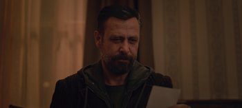 Movie still from “10 Days of a Good Man” (2023), directed by Uluç Bayraktar – A man with a goatee looking at a piece of paper; Close Up shot, Over the shoulder angle