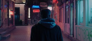 Movie still from “10 Days of a Good Man” (2023), directed by Uluç Bayraktar – A man wearing a hoodie walking down a street; Medium shot, Low angle