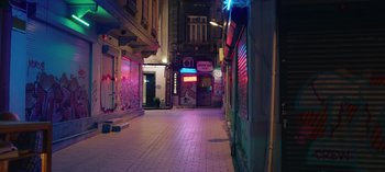 Movie still from “10 Days of a Good Man” (2023), directed by Uluç Bayraktar – An alley way with neon signs lit up at night; Extreme Wide shot, High angle