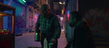 Movie still from “10 Days of a Good Man” (2023), directed by Uluç Bayraktar – A man pouring a drink into a cup while another man watches; Medium shot, Over the shoulder angle