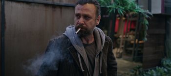 Movie still from “10 Days of a Good Man” (2023), directed by Uluç Bayraktar – A man smoking a cigarette while wearing a jacket; Close Up shot, Over the shoulder angle
