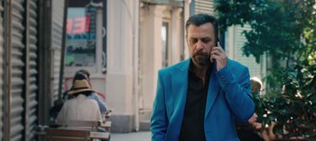 Movie still from “10 Days of a Good Man” (2023), directed by Uluç Bayraktar – A man in a blue suit talking on a cell phone; Medium shot, Over the shoulder angle