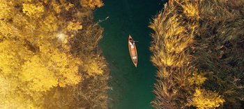 Movie still from “10 Days of a Good Man” (2023), directed by Uluç Bayraktar – An aerial view of a boat floating on a river; Extreme Wide shot, Overhead angle
