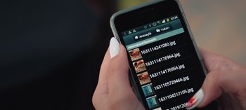 Movie still from “10 Days of a Good Man” (2023), directed by Uluç Bayraktar – A hand holding a cell phone with a bunch of pictures on it; Extreme Close Up shot, High angle