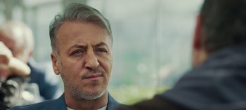 Movie still from “10 Days of a Good Man” (2023), directed by Uluç Bayraktar – A person wearing a suit and tie; Close Up shot, Over the shoulder angle