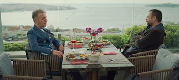 Movie still from “10 Days of a Good Man” (2023), directed by Uluç Bayraktar – People are sitting at an outdoor table with wine glasses; Wide shot, Low angle