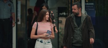 Movie still from “10 Days of a Good Man” (2023), directed by Uluç Bayraktar – A woman holding a cell phone while standing next to a man; Medium shot, Over the shoulder angle