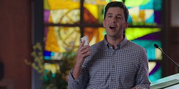 Movie still from “13: The Musical” (2022), directed by Tamra Davis – A man holding a cell phone in his hand; Medium shot, Over the shoulder angle