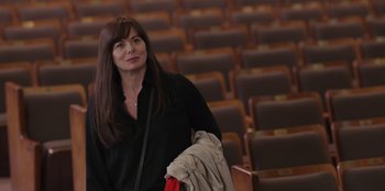 Movie still from “13: The Musical” (2022), directed by Tamra Davis – A woman standing in front of rows of chairs; Medium shot, Over the shoulder angle