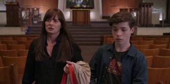 Movie still from “13: The Musical” (2022), directed by Tamra Davis – A woman standing next to a young boy in front of a staircase; Medium shot, Over the shoulder angle