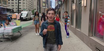 Movie still from “13: The Musical” (2022), directed by Tamra Davis – A young boy standing on the side of the street; Medium shot, Over the shoulder angle