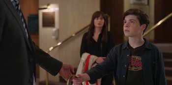 Movie still from “13: The Musical” (2022), directed by Tamra Davis – A young man is handing a coin to a woman; Medium shot, Over the shoulder angle