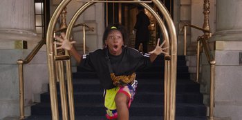 Movie still from “13: The Musical” (2022), directed by Tamra Davis – A young girl is standing in a golden cage; Medium shot, High angle