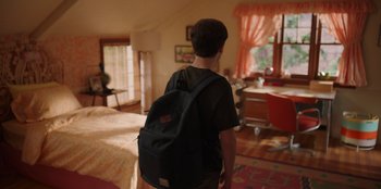 Movie still from “13: The Musical” (2022), directed by Tamra Davis – A man with a backpack standing in a bedroom; Wide shot, High angle