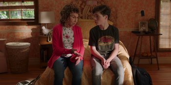 Movie still from “13: The Musical” (2022), directed by Tamra Davis – A woman and a young boy sitting on a couch; Medium shot, Over the shoulder angle