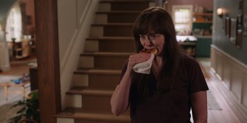 Movie still from “13: The Musical” (2022), directed by Tamra Davis – A woman eating a piece of bread on the stairs; Medium shot, Over the shoulder angle