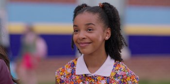 Movie still from “13: The Musical” (2022), directed by Tamra Davis – A young girl smiles brightly while wearing a floral dress; Close Up shot, Over the shoulder angle