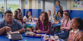 Movie still from “13: The Musical” (2022), directed by Tamra Davis – A group of people sitting at a table eating food; Medium shot, Over the shoulder angle