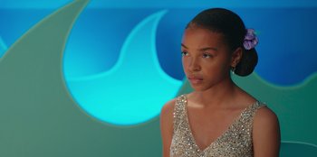 Movie still from “13: The Musical” (2022), directed by Tamra Davis – A woman in a silver dress is standing in front of a blue background; Close Up shot, Over the shoulder angle
