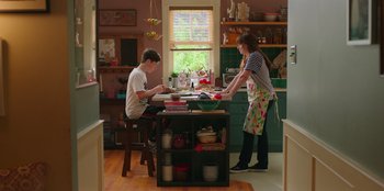 Movie still from “13: The Musical” (2022), directed by Tamra Davis – A man and a woman preparing food in a kitchen; Wide shot, High angle