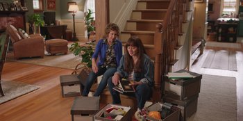 Movie still from “13: The Musical” (2022), directed by Tamra Davis – Two women sitting on the steps of a house; Wide shot, High angle