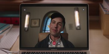 Movie still from “13: The Musical” (2022), directed by Tamra Davis – A man is smiling for the camera while sitting in front of a computer screen; Close Up shot, Over the shoulder angle