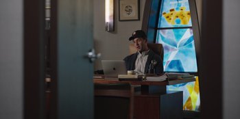 Movie still from “13: The Musical” (2022), directed by Tamra Davis – A man sitting at a desk using a laptop computer; Medium shot, Low angle